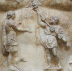 Marble carving of a breastplate on a statue depicting a scene with one man standing and gesturing, while another man kneels before him.