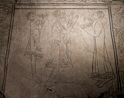 A carved stone floor with black outlines of a man, woman, and their son, arms raised and looking up to God. The style of art is Romanesque.