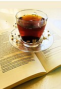 Glass cup holding black tea on a small glass plate, sitting on a book