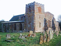 A stone church seen from the northwest with a squat tower in the foreground, with the north aisle to the left and the west end of the nave to the right