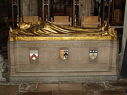 A stone rectangular monument, with the golden figure of a man dressed in robes and wearing a mitre lying on top, with his hands together in a gesture of prayer. The words "Edward Stuart Talbot" on the side in gold, with three shields bearing coats of arms below.  At the bottom, in gold: beneath the first shield, "1870 Keble 1888"; beneath the second, "1834–1944"; beneath the third, "1889 Leeds 1895"
