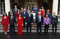 Sanchez wearing a suit and red tie standing with his cabinet surrounding him