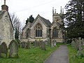 Gray three bay building with arched windows. Tower behind and gravestones in the foreground.