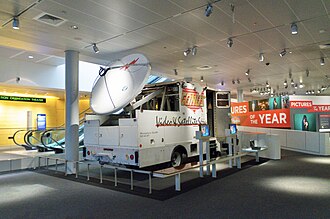A large trailer truck with a satellite dish mounted on its rear and CONUS logo on its side inside a museum.