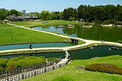 Garden with dried grassland, plants, woods and a large pond with islands.
