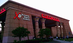 The entrance to a Cinemark movie theater with the text on the left "Extreme Digital Cinema". A red X and a white D is next to that specific text.