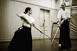 A woman and a man doing marshal arts with long sticks