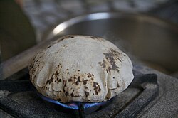 A flatbread directly over a gas stove. It is ballooning to a high height.