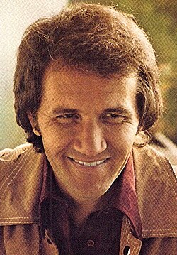 A brown-haired man wearing a tan jacket