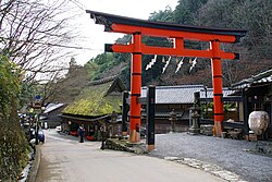 Large red torii next to a wooden thatched house.