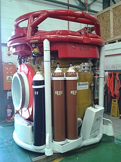 Side view of a closed bell showing the side hatch and cylinders for emergency gas supply of heliox and oxygen.