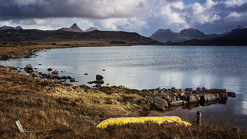 Upturned boat on Loch Osgaig. Looking at the right is the  twin peaks of Sgorr Tuath and Sgorr Deas. In the middle is the foreground peak of Stac Pollaidh to the left and Cùl Beag behind. To the left is the peak of Cùl Mòr