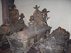 Three grey, ornamental sarcophagi standing next to each other, with a fourth underneath the one in the centre