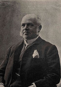 An old man with white hair and sideburns wearing a suit