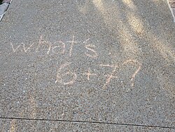 A photo of a sidewalk with chalk writing that reads "What's 6+7?"
