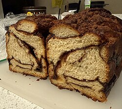 Cinnamon babka with streusel topping on cutting board, cut cross-wise to reveal streaks of cinnamon filling throughout.