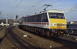 A Class 90, which is a parallelogrammical prism shape, in service. Because of the angle only the locomotive and a bit of its first coach are visible. The colour photo is taken from the track below, looking slightly up.