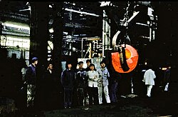 A group of workers pose next to heavy machinery, including a glowing ball of metal