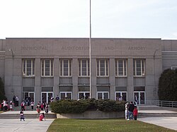 The entrance of a concrete building behind a front lawn and a flag pole