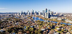 An arial photograph of a large city, a suburban area can be seen in the foreground while numerous skyscrapers fill the near skyline