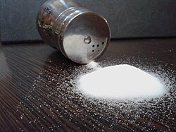 A small pile of white crystals in front of a tipped-over cylindrical with a few grains spilling out of the holes in its screw-top lid