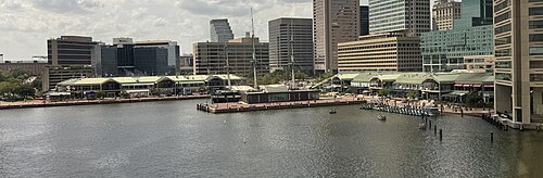 A panorama of the Harborplace promenade/waterfront in the Inner Harbor, featuring two small malls with green roofs, the Pratt Street Pavilion (left, alongside a blue-green building known as The Gallery at Harborplace) and the Light Street Pavilion (middle right).
