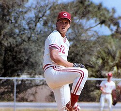 A man wearing a white baseball uniform and a red cap with a white "C" on the front prepares to pitch a baseball.