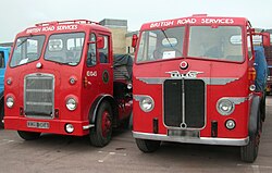 Two old-fashioned red vehicles, with the photo taken from almost the front. They have large grills and big windows with a middle bar. On top of their front windows it says "BRITISH ROAD SERVICES"