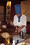 A Teppanyaki chef cooking at a hibachi in a Japanese Steakhouse.