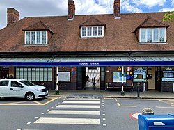 A brown-bricked building with four brown-bricked chimneys and a rectangular, dark blue sign reading "STANMORE STATION" in white letters
