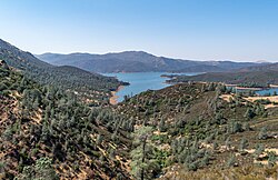 View of Lake McClure reservoir, with chaparral-covered foothills under blue sky