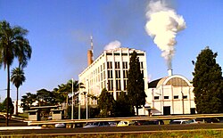Photo of shorter building with smoke coming out of smokestack next to five-story office building