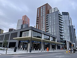 A low grey building with a projecting canopy stands in front of tall residential buildings