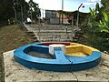A monument in Laman Tiga Budaya, marking the tripoint between the states of Malacca (red), Negeri Sembilan (yellow) and Johor (blue), with the water theme park in the background.