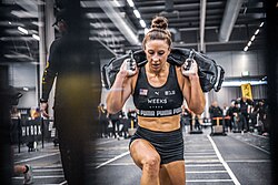 Lauren Weeks, a muscular white woman, competing in Hyrox in a lunge carrying weights on her back