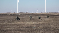 Russian servicemen demining an area in front of wind power plants and next to dragon teeth.