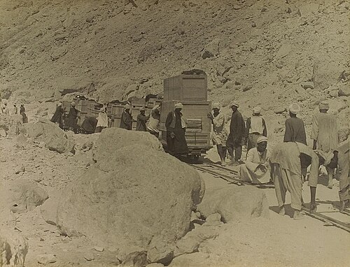A crowd of workers pushing rail cars along tracks while others lay more tracks in front