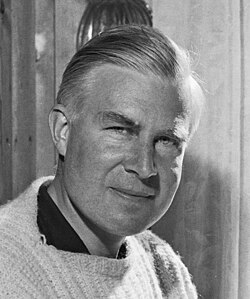 Black-and-white photo of a man with combed hair wearing a knit sweater over a dark shirt