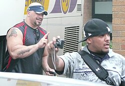 Two adult Hispanic males wearing hats posing for a photograph.