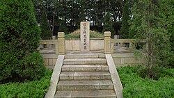 A photo of Gu Yanwu's grave, taking the form of a stele in front of an earthen mound. It is surrounded by foliage, with a stone stairway leading up to it.