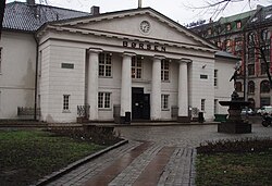 Photograph showing the main entrance to the Oslo Børs, known in English as the Oslo Stock Exchange in Norway.  The building is in the Renaissance architectural style, its exterior painted in an Ivory white colour.  Its entrance is protected by an imposing porch topped with a triangular pediment supported by four columns.