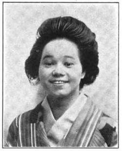 A smiling young Japanese-American woman, with dark hair in a bouffant style, wearing a striped kimono