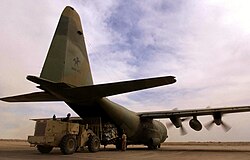 Rear view of a propeller-driven plane on the ground with its cargo door open and propellers still spinning