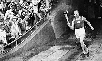 Paavo Nurmi enters the Helsinki Olympic Stadium carrying the torch during the opening ceremonies. He became the first well-known athlete to light the Olympic Flame.