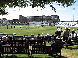 Photograph of the County Cricket Ground in Hove, showing benches in the foreground and the cricket field beyond that