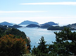 A clear bright ocean sparkling with light, dotted with several small forested islands.