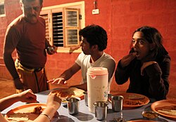 People with plates of chapati and another food. One of them holds a torn piece of chapati to eat.