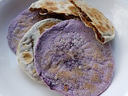 Two types of flatbreads. One is purple with seeds on the surface. The other is golden-brown and cut to show a dark filling.