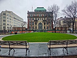 stone courthouse building with grassy circular park in front of it, surrounded by benches