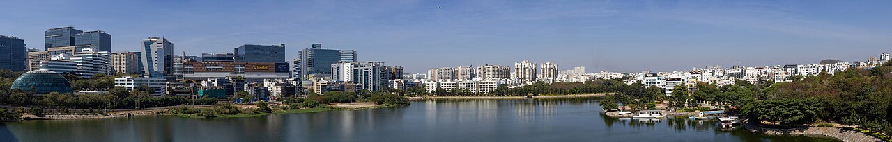 Panoramic view of a lake with high rise glass office buildings on the left and low-rise residential buildings on its right.